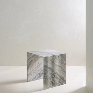 May include: A square marble side table with a gray and white color scheme. The table has a textured, striped design on the sides and a smooth top. The table is a modern piece of furniture.