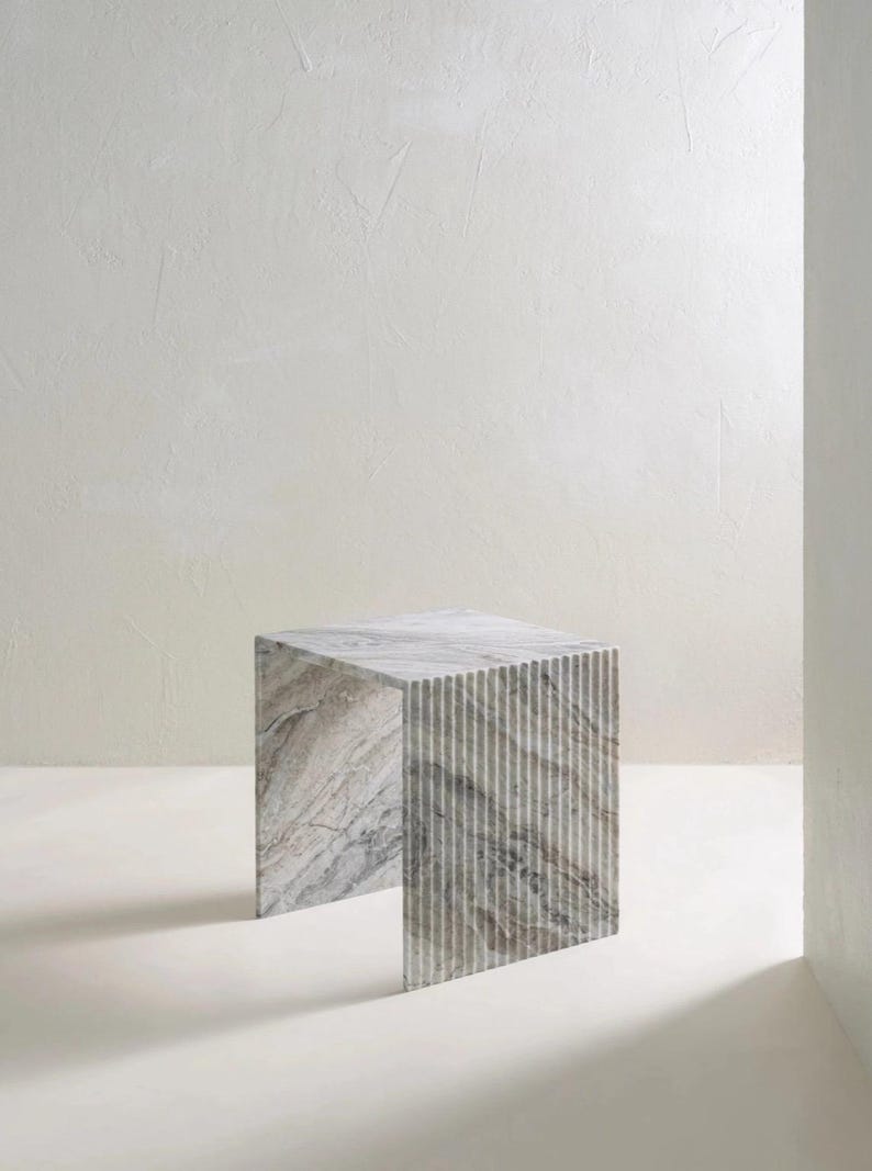 May include: A square marble side table with a gray and white color scheme. The table has a textured, striped design on the sides and a smooth top. The table is a modern piece of furniture.