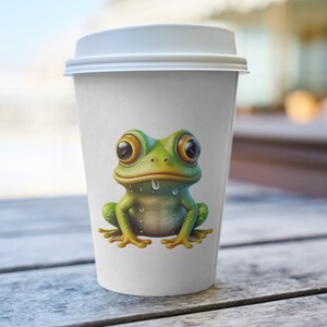 May include: A white to-go coffee cup with a green frog with large eyes and a dripping mouth printed on the front.