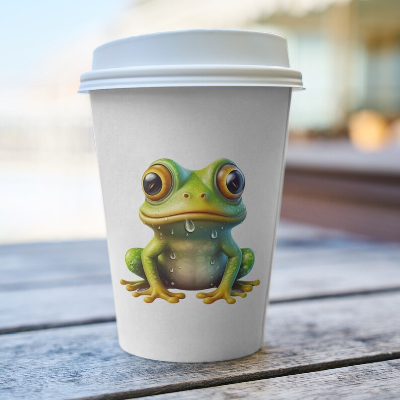 May include: A white to-go coffee cup with a green frog with large eyes and a dripping mouth printed on the front.