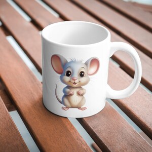 May include: White ceramic mug with a cartoon illustration of a cute gray mouse with big eyes and a pink nose. The mouse is standing on its hind legs with its paws together.