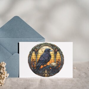 May include: A black raven perched on a book in a stained glass window with a sunset background. The window is round and has a gold frame. The raven is looking to the right.