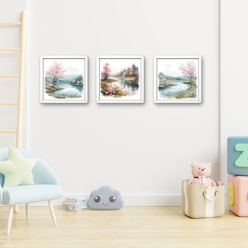 以下が含まれることがあります： 木々、川、ピンクの花が描かれた風景画が、白い額縁に収められています。3つの絵画は白い壁に飾られています。