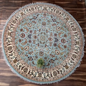 Może przedstawiać: Okrągły dywan w kolorze niebieskim i kremowym z kwiatowym wzorem. Dywan ma frędzlowaną krawędź.