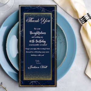 May include: A navy blue and gold birthday thank you card with the text "Thank You" and "40th Birthday". The card has a marble design and is placed on a blue plate with a napkin and silver ring.