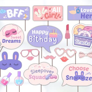 May include: A set of 12 pink and purple photo booth props with various designs, including a bunny wearing a sleep mask, a pair of glasses, a moustache, a bow, a lipstick, a bottle of nail polish, a cake, a sleeping mask, a speech bubble that says "Happy Birthday", a speech bubble that says "Sweet Dreams", a speech bubble that says "Choose Snooze", a speech bubble that says "Sleepover Squad", a speech bubble that says "All Girl!" a speech bubble that says "Love Her", a speech bubble that says "BFF", and a speech bubble that says "Snacks".