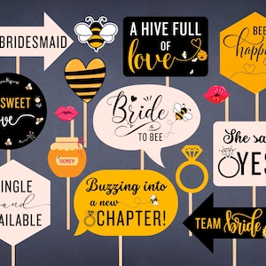 May include: A set of 12 bee-themed photo booth props for a bridal shower or wedding. The props feature phrases like "Bride to Bee", "A Hive Full of Love", and "She Said Yes!" with bee and honeycomb designs.