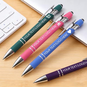 May include: Four ballpoint pens in various colours: green, pink, blue, and purple. Each pen has silver detailing and a black tip. The text "YOUR TEXT/LOGO HERE" is printed on each pen, along with small icons.