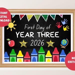 Peut inclure: Impression encadrée de style tableau noir avec le texte "First Day of YEAR THREE 2026". Le design comprend un soleil, une pomme, des étoiles, un globe, des empreintes de mains, des crayons et une bannière. Cercles rouges et jaunes avec du texte dans les coins.