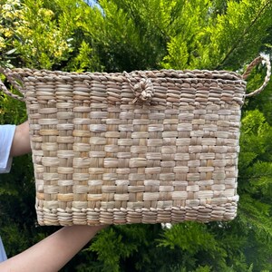 Könnte beinhalten: Ein geflochtener Korb mit zwei Griffen und einem geknoteten Verschluss. Der Korb ist aus natürlichen Materialien gefertigt und hat eine hellbraune Farbe.