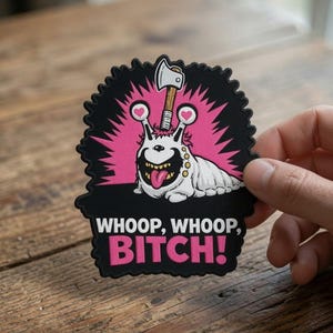 May include: A die-cut sticker featuring a white slug-like creature with a single eye, a wide grin, and an axe embedded in its head. The background is black with pink radiating lines. The text reads WHOOP, WHOOP, BITCH! in white and pink letters.