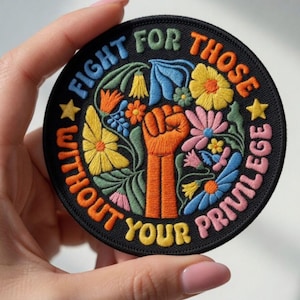 May include: Embroidered patch with the text "FIGHT FOR THOSE WITHOUT YOUR PRIVILEGE" in various colors. The patch features a raised fist and colorful flowers on a black background.