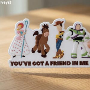 以下が含まれることがあります： アニメ映画「トイ・ストーリー」のキャラクターが描かれた刺繍パッチ。パッチにはボー・ピープ、茶色の馬、ウッディ、バズ・ライトイヤーが含まれています。「YOU'VE GOT A FRIEND IN ME」のフレーズが茶色のテキストで下部に印刷されています。