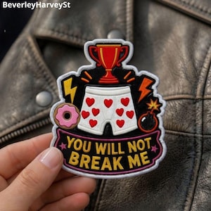 May include: An embroidered patch featuring a white pair of boxer shorts with red hearts, a red trophy, a pink donut, a yellow lightning bolt, an orange lightning bolt, and a bomb. The text reads YOU WILL NOT BREAK ME in yellow capital letters.