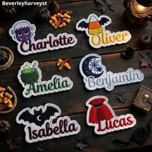 Könnte beinhalten: Sechs bestickte Namensaufnäher mit Halloween-Motiven: ein lila Monster für Charlotte, ein Zuckermais für Oliver, ein grüner Kessel für Amelia, ein Mond mit Spinnennetz für Benjamin, eine schwarze Fledermaus für Isabella und ein roter Umhang für Lucas.