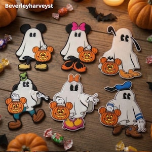 Könnte beinhalten: Sechs bestickte Aufnäher mit Zeichentrickfiguren, die als Geister für Halloween verkleidet sind. Jede Figur trägt ein weißes Laken und hält einen orangefarbenen Kürbiseimer mit mausohrähnlichen Griffen. Die Figuren zeigen Variationen mit Schleifen, Hüten und Schuhen.