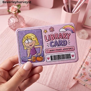 Peut inclure: Un écusson brodé rectangulaire dans des tons rose et violet représentant un personnage de dessin animé aux cheveux blonds, le texte LIBRARY CARD, un arc-en-ciel, une fleur, une étoile et la phrase BOOKS. FRIENDS. ADVENTURES. avec un code-barres.