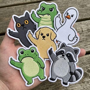Puede incluir: Parches bordados con varios animales, incluyendo un gato negro, un caimán, un perro, un pato, una rana y un mapache, cada uno mostrando el dedo medio. Los parches tienen bordes blancos. El texto "Beverleyharveyst" es visible.