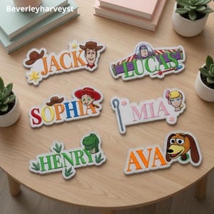 May include: Six embroidered name patches featuring Toy Story characters. The patches display the names Jack, Lucas, Sophia, Mia, Henry, and Ava, each accompanied by a character illustration including Woody, Buzz Lightyear, Jessie, Bo Peep, Rex, and Slinky Dog.