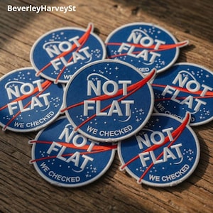 Puede incluir: Un conjunto de parches redondos azules con el texto blanco "NOT FLAT" y un diseño rojo. Los parches también incluyen el texto blanco "WE CHECKED". Los parches están colocados sobre una superficie de madera.