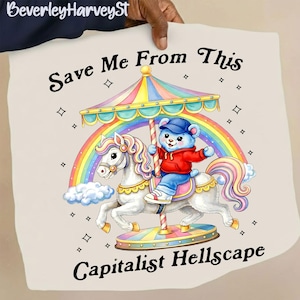 May include: A cream-colored graphic featuring a carousel scene with a blue bear wearing a red hoodie and a blue cap riding a white unicorn. The carousel has a rainbow-colored canopy and a rainbow in the background. Text reads "Save Me From This Capitalist Hellscape."