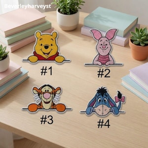 May include: Four embroidered character patches featuring Winnie the Pooh, Piglet, Tigger, and Eeyore. Each patch shows the character peeking over a horizontal line. The patches are labelled #1, #2, #3, and #4 respectively, with vibrant colours.