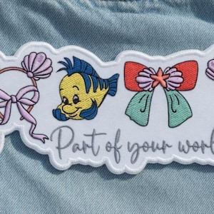 Op de afbeelding: Een wit geborduurd embleem met cartoonafbeeldingen van een vis, strikken en haarbanden met schelpaccenten. De patch bevat de tekst "Part of your world" in een cursief lettertype, alles tegen een lichtblauwe denim achtergrond.