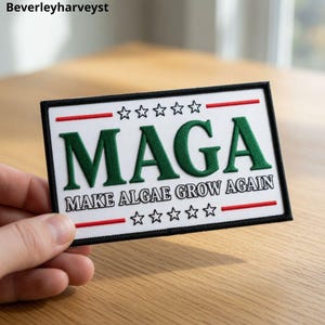 Peut inclure: Un écusson rectangulaire brodé sur fond blanc avec une bordure noire. Le texte MAGA est écrit en grandes lettres vertes, avec les mots MAKE ALGAE GROW AGAIN en plus petites lettres noires en dessous. Deux lignes rouges et dix étoiles figurent.