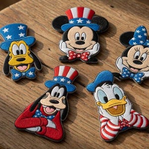 Könnte beinhalten: Eine Sammlung von aufgestickten Aufnähern mit beliebten Zeichentrickfiguren, darunter Micky Maus, Minnie Maus, Goofy und Donald Duck. Jeder Aufnäher ist mit patriotischen roten, weißen und blauen Farben und festlichen Hüten verziert.