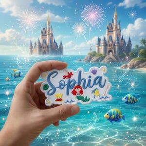 Pode incluir: Um patch branco com o nome "Sophia" em azul, com ilustra&ccedil;&otilde;es de desenhos animados de uma sereia, peixes e outros elementos marinhos. O patch &eacute; mostrado em frente a uma paisagem com um castelo, o oceano e fogos de artif&iacute;cio.