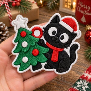 Puede incluir: Un parche bordado que muestra un gato negro con un gorro de Papá Noel rojo y una bufanda roja, junto a un árbol de Navidad verde decorado con adornos circulares rojos y blancos y rematado con una estrella blanca, todo con borde blanco.