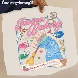 May include: Cream-colored graphic tee featuring the text "Fauna Bakery" in pink script, with illustrations of a blue cake, birds, and fairies. The design includes the text "Baked with Love & Magic" and "Once Upon A Dream."