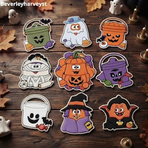 Puede incluir: Una colección de nueve adornos planos con temática de Halloween que presentan personajes de dibujos animados, incluyendo un cubo verde, un fantasma, un cubo de calabaza naranja, una momia, una calabaza central, un cubo morado, un cubo fantasma, una bruja y un vampiro.