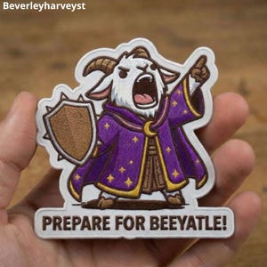 May include: An embroidered patch featuring a white goat character wearing a purple robe with yellow stars, holding a brown shield, and pointing upward. The text at the bottom reads PREPARE FOR BEEYATLE! The design has a white border and stitching.