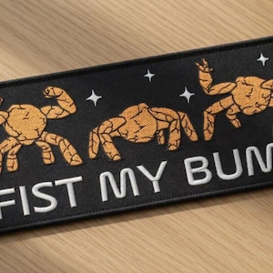 May include: Black rectangular patch with the text "FIST MY BUMP" in white. The patch features three orange crab illustrations with flexed arms and star accents. The brand name "BEVERLEYHARVEYST" is at the top left.