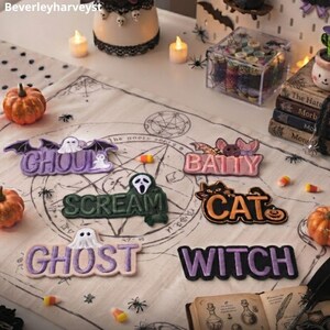 May include: A collection of six embroidered patches featuring Halloween-themed words and characters. The patches include the words GHOUL, BATTY, SCREAM, CAT, GHOST, and WITCH, each accompanied by corresponding icons like a ghost, bat, mask, cat, and pumpkin.