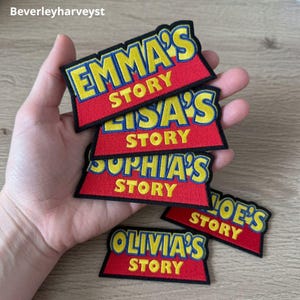 May include: A collection of embroidered patches featuring a red trapezoidal base with yellow text. The patches display various names followed by the word STORY in yellow capital letters. The text is outlined in blue, and the patches have black borders.