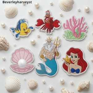Può includere: Una collezione di toppe ricamate raffiguranti un pesce giallo, un granchio rosso, una barriera corallina rosa, una conchiglia rosa con una perla, un tritone con un tridente dorato e una sirena dai capelli rossi con una stella marina gialla, circondati da conchiglie bianche.