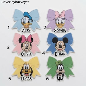 May include: Six embroidered patches shaped like bows, each featuring a Disney character face and a name. Characters include Donald Duck, Daisy Duck, Minnie Mouse, Mickey Mouse, Pluto, and Goofy, with names Alex, Sophia, Olivia, Ethan, Lucas, and Mia.
