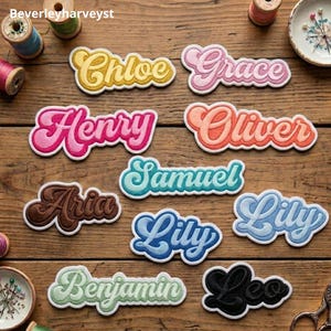 以下が含まれることがあります： Chloe、Grace、Henry、Oliver、Samuel、Aria、Lily、Benjamin、Leoという名前が刺繍された、様々な色とフォントのワッペン。木製の表面に、糸巻きや針山と一緒に配置されています。