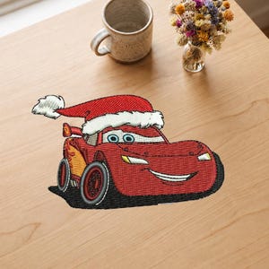Puede incluir: Un parche bordado que muestra un coche de carreras rojo con ojos azules y una amplia sonrisa, usando un gorro de Papá Noel rojo y blanco. El coche tiene gráficos de rayos amarillos en el lateral, neumáticos negros y un pequeño alerón trasero.