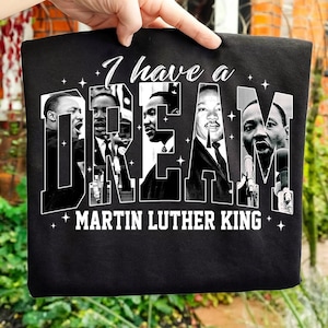 May include: Black t-shirt with a white graphic design. The words "I have a DREAM" are displayed, with images of Martin Luther King Jr. integrated into the letters. The text "MARTIN LUTHER KING" is printed below the main text.