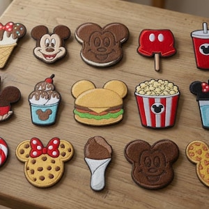 May include: A collection of fourteen embroidered patches featuring various food items and character-themed designs. The set includes ice cream cones, Mickey Mouse faces, a burger, popcorn, a lollipop, a cookie, and drinks, all with colourful thread details.