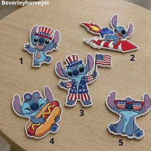 Könnte beinhalten: Fünf gestickte Aufnäher mit der blauen Figur Stitch in verschiedenen patriotischen Posen. Die Motive zeigen Stitch mit Zylinder, auf einer Rakete reitend, mit einer amerikanischen Flagge, beim Essen eines Hotdogs und mit einer Flaggenbrille.