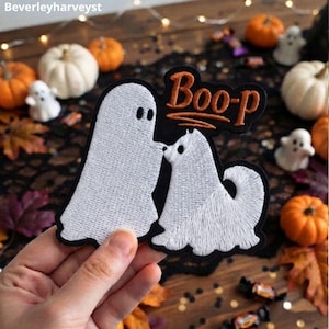 May include: An embroidered patch featuring a white ghost and a white dog facing each other on a black background. The text "Boo-p" is stitched in orange above the figures. The design is shaped to follow the outlines of the ghost and the dog.