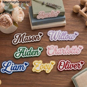 Könnte beinhalten: Eine Sammlung bestickter Namensaufnäher mit den Namen Amelia, Mason, Willow, Aiden, Charlotte, Liam, Zoey und Oliver. Jeder Aufnäher hat eine Schreibschrift, einen weißen Rand und ein kleines Herzsymbol am Ende des Namens.