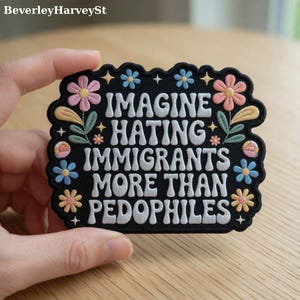 May include: Black embroidered patch with the text "IMAGINE HATING IMMIGRANTS MORE THAN PEDOPHILES" in white. The patch is decorated with colorful flowers and stars around the edges.