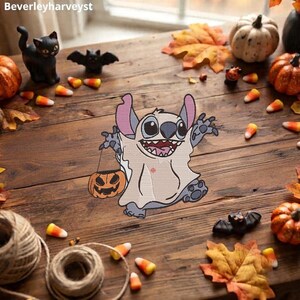 Puede incluir: Un parche bordado que muestra a un personaje alienígena azul con un disfraz de fantasma blanco, sosteniendo un pequeño cubo naranja de calabaza. El personaje tiene orejas grandes, una sonrisa amplia con dientes y una pose juguetona.