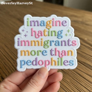 Pode incluir: Patch bordado com o texto "imagine hating immigrants more than pedophiles" em letras coloridas costuradas. O patch tem uma borda branca e é segurado por uma mão.
