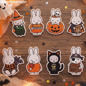 May include: A set of eight embroidered patches featuring white rabbits and a black cat in various Halloween costumes, including a witch, a vampire, a pirate, and a pumpkin. The designs include accessories like a cauldron, pie, and treasure chest.